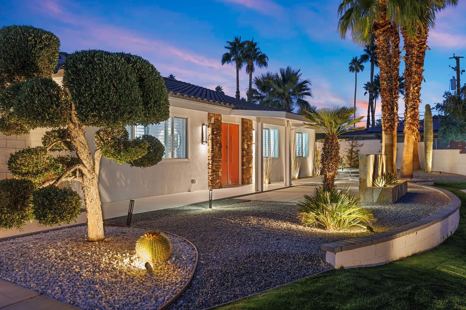Sculpted trees and orange double doors welcome you home, with landscape lighting that comes on every evening.