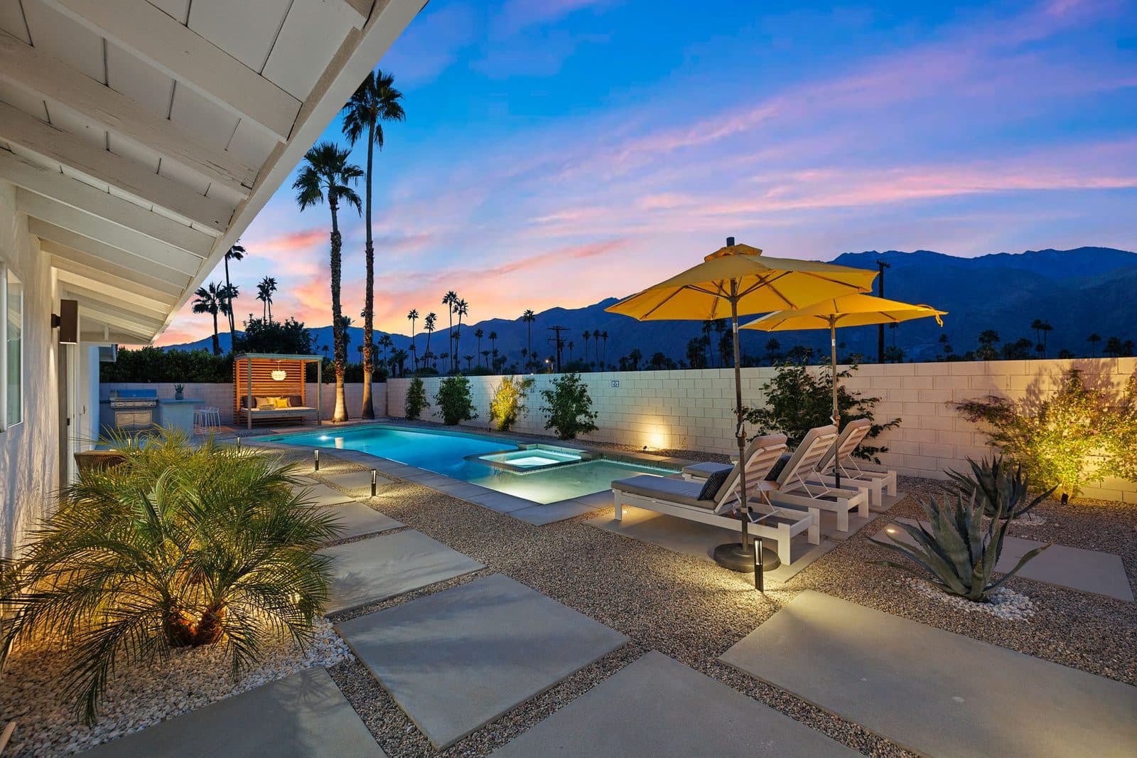 Sunset over the San Jacintos from the pool deck. Loungers and umbrellas line one side, with the cabana daybed and grill at the far end.